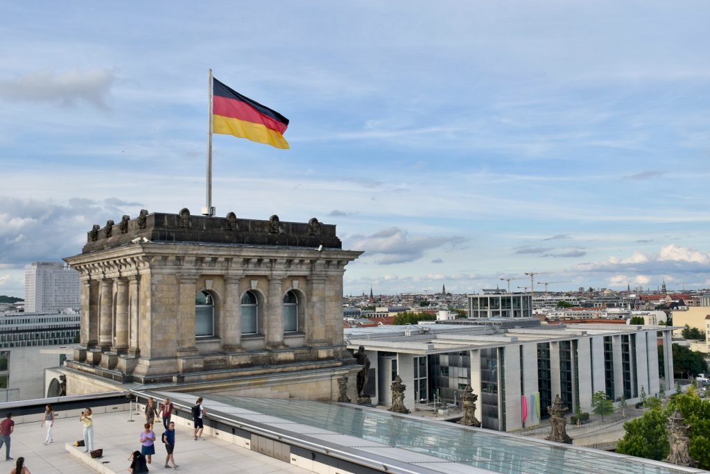 German flag flies at the top of a building with a rooftop patio overlooking cityscape