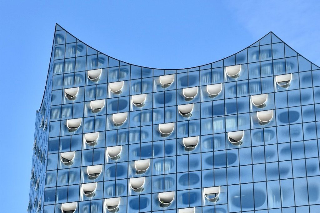 A modern building made of blue glass shaped like waves at the top. White detailing on some windows