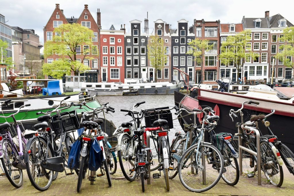 Row of Dutch canal houses across the top of the photo, then layer of canal boats, then grey river. Row of bicycles in the foreground