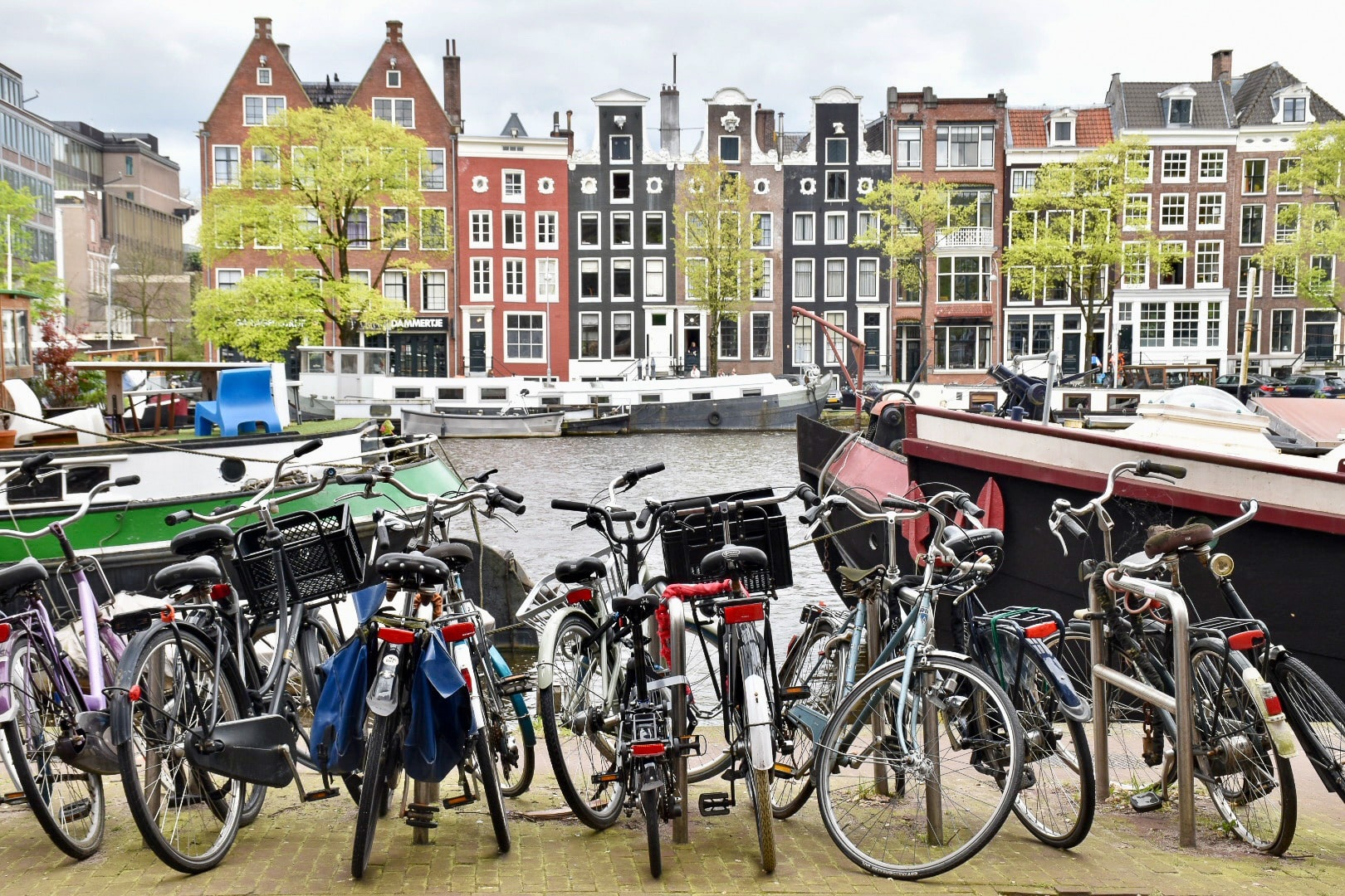 Row of Dutch canal houses across the top of the photo, then layer of canal boats, then grey river. Row of bicycles in the foreground