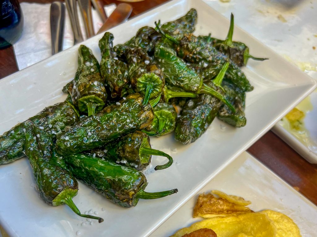 White rectangular plate on a table top, filled with a heap of fried green padron peppers