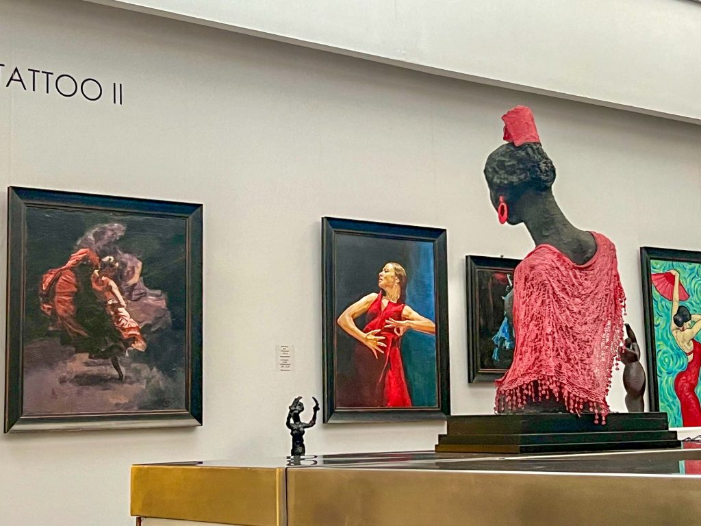 View of museum exhibits which all feature flamenco scenes on the paintings on the wall. To the right hand side is a sculpture wearing a pink lace shawl (looking away from the camera)