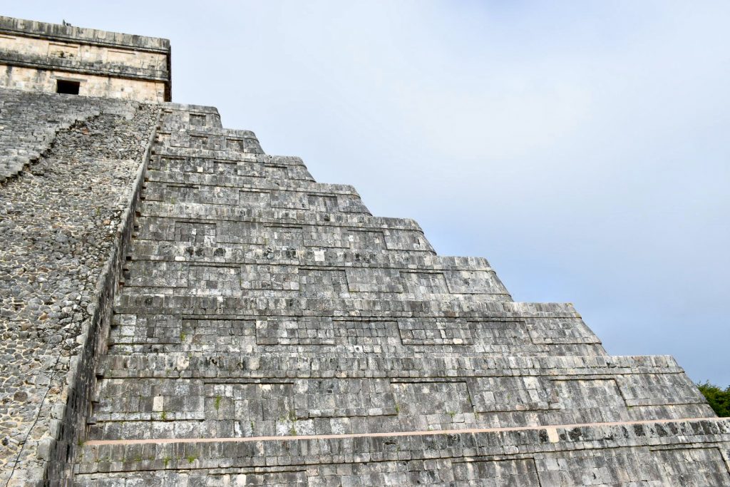 Looking up at the top of a stone stepped pyramid from near its top. The pyramid has a square structure at the top