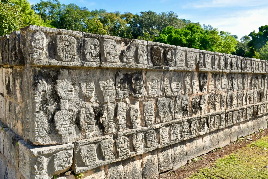 A long stone platform featuring rows of carvings of skulls. Trees behind
