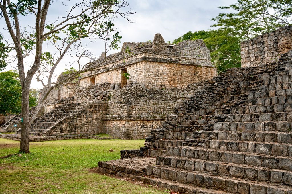View from the right hand side of stepped stone temple buildings or platforms. One in the foreground, one in the middle and one in the distance. Trees behind and to the left