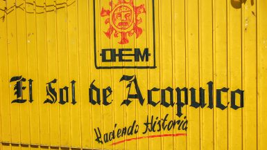 A bright yellow container with black printed words 'El Sol de Acapulco, Hacienda Historia'
