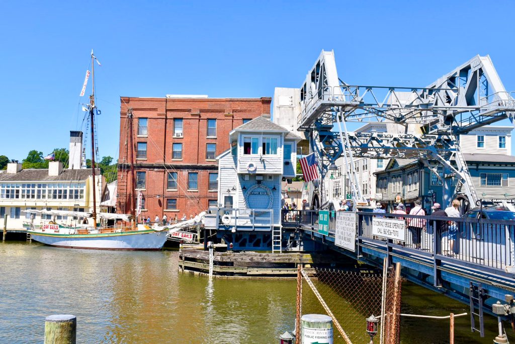 Looking across a pale grey bridge to the buildings on the other side. It looks heavily mechanical as if a drawbridge. Red brick building on the far side.