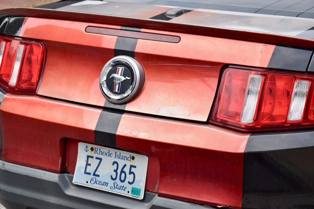 Image of the back of a red sports car with a hose logo on the back. Registration plate for Rhode Island, Ocean State