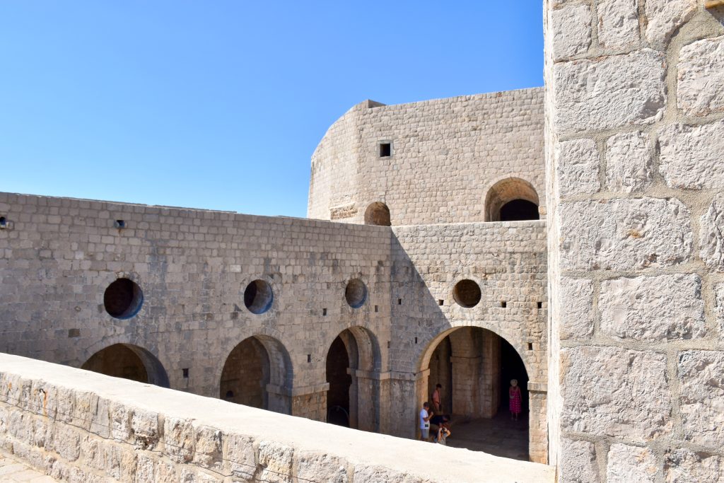 On the walls of a white stone fortress looking into an inner courtyard with arches around the edges. Blue sky above