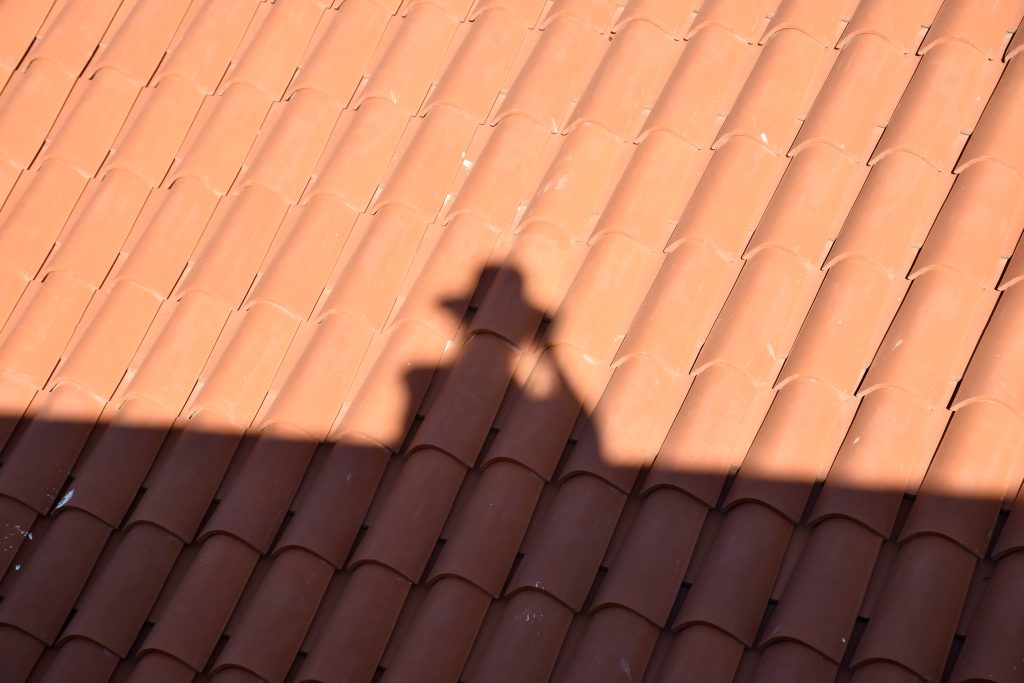 A shadow is cast by the sun of a person in hat, on terracotta roof tiles