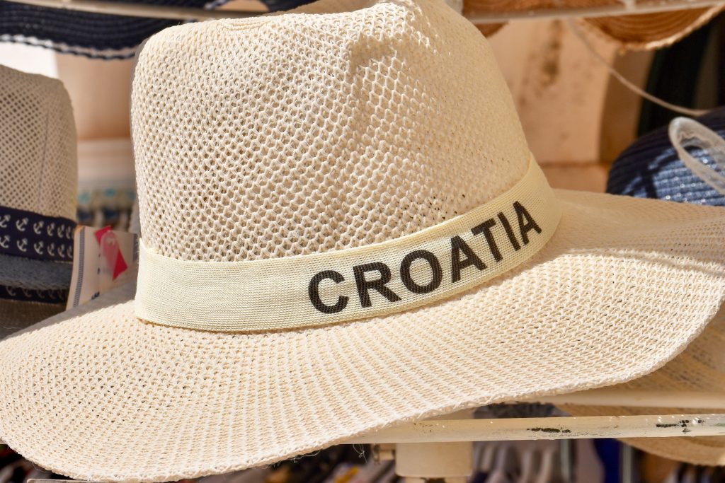A display of straw hats sits outside a clothes shop. The straw hat in front has a ribbon around the brim which says Croatia on it.