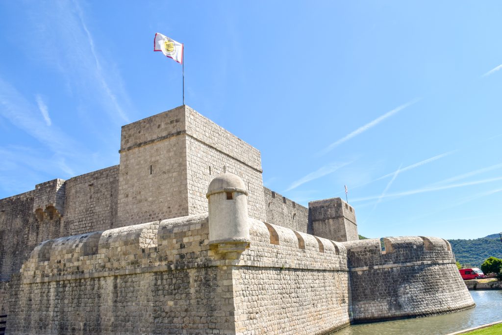 A large fortress building with a moat sits in the middle of the frame. It is flying a flag. Pale blue sky above
