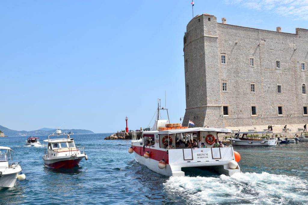 View of small boats entering and leaving a port with tall stone fortress building to the right.