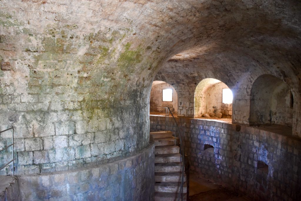Inside a circular stone building with vaulted roof and arched windows. A stone staircase curves around a pillar in the middle
