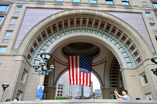 A large archway is built into a modern building which is flying the Stars and Stripes from its ceiling. A man in the foreground takes a photo on his mobile phone