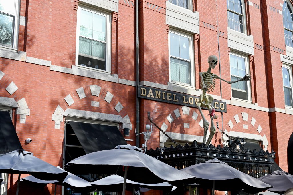 Red brick building with a Skeleton standing up on the top of a black doorway which has the words Rockafellas on it. Row of black umbrella parasols along the bottom