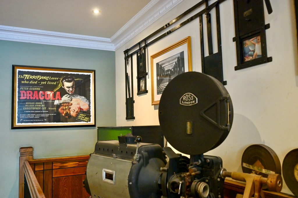 Inside a room with a framed Dracula movie poster on the wall to the left and an old cine camera to the right hand side.