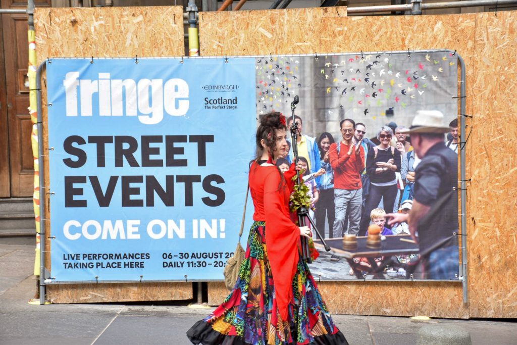 Lady in red dress which looks Spanish walking past a large bill poster advertising street Events