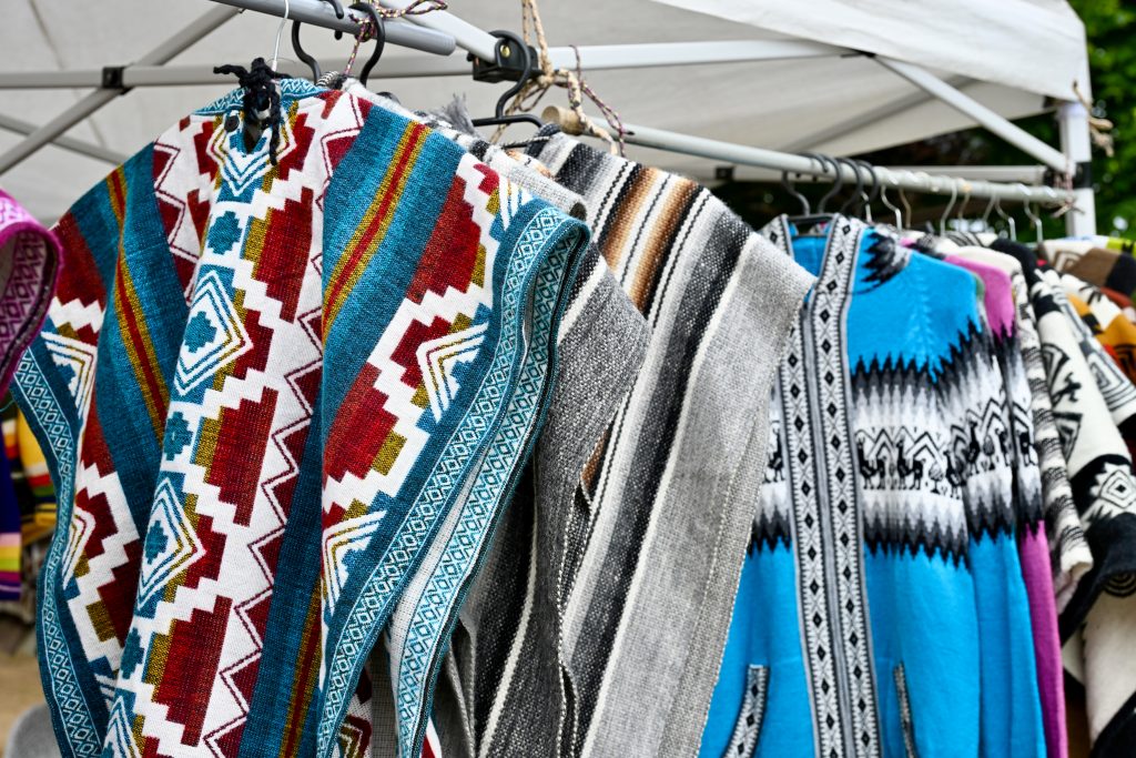 A line of woven ponchos hangs from left to right under a cream canvas of an open air market