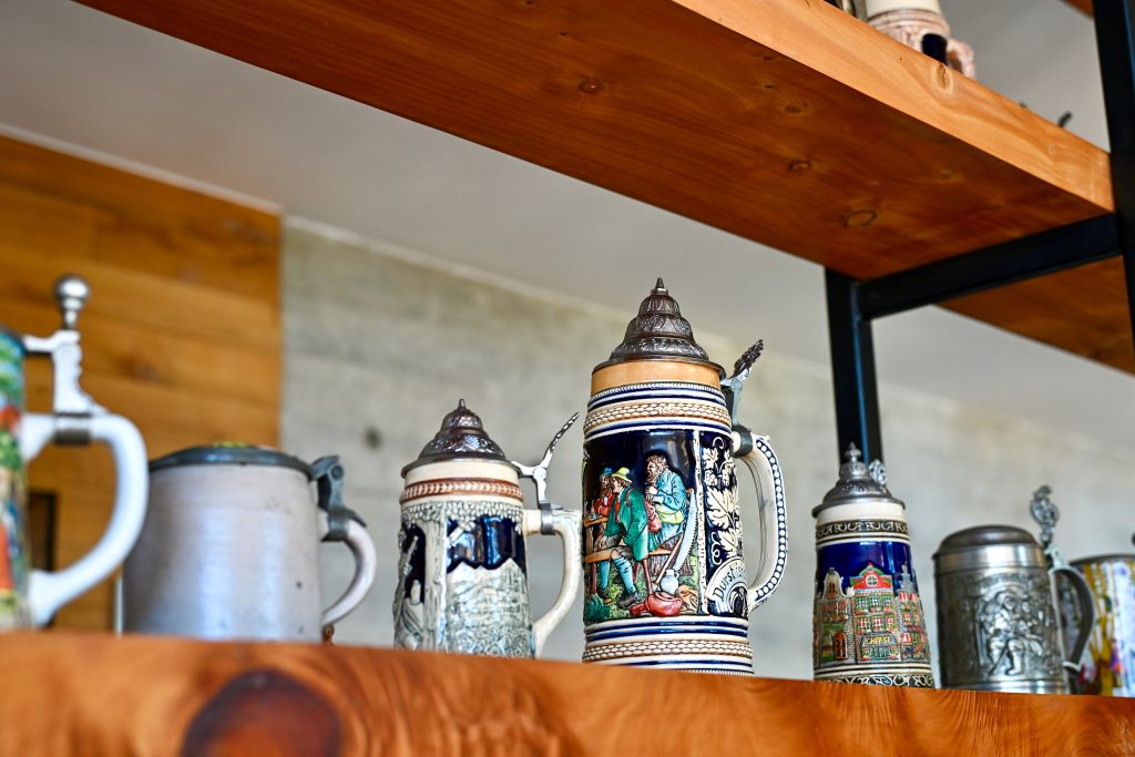 Two wooden shelves run across the frame from left to right. There is a row of German Bavarian beer tankards with silver lids sitting on the shelves