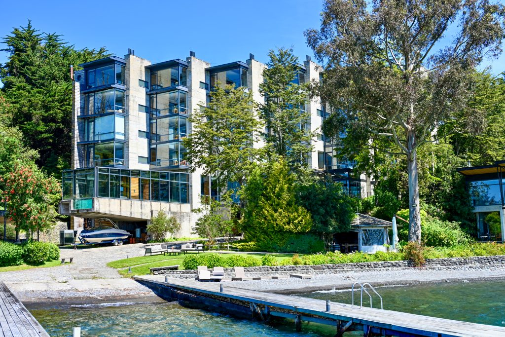 View from a pier looking back towards a modern concrete building with glass windows in layered block style. Trees either side