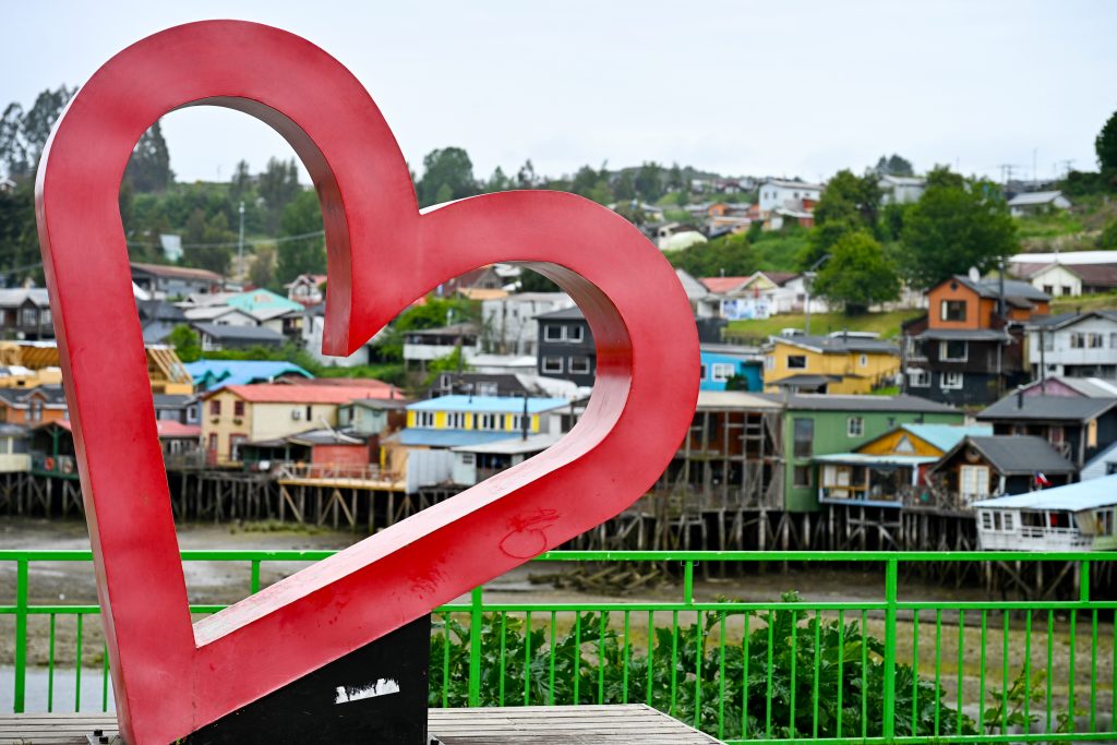 Rows of multicoloured houses line a hill in the background. It has a red heart to the left hand side.