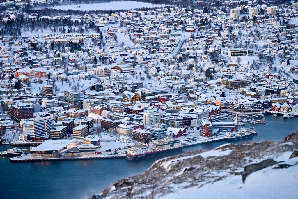 Looking down on a city with tightly packed houses and buildings surrounded by snow. Body of water in the foreground