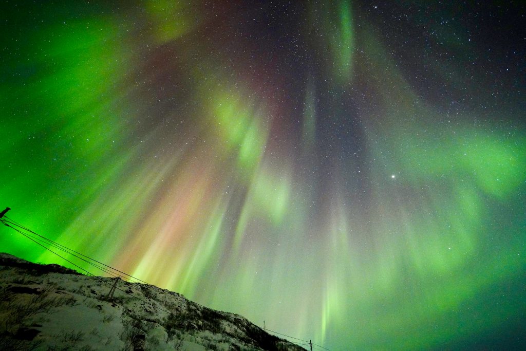 Rays of green, purple and red right radiate from top right corner. Silhouette of snowy hillside bottom left