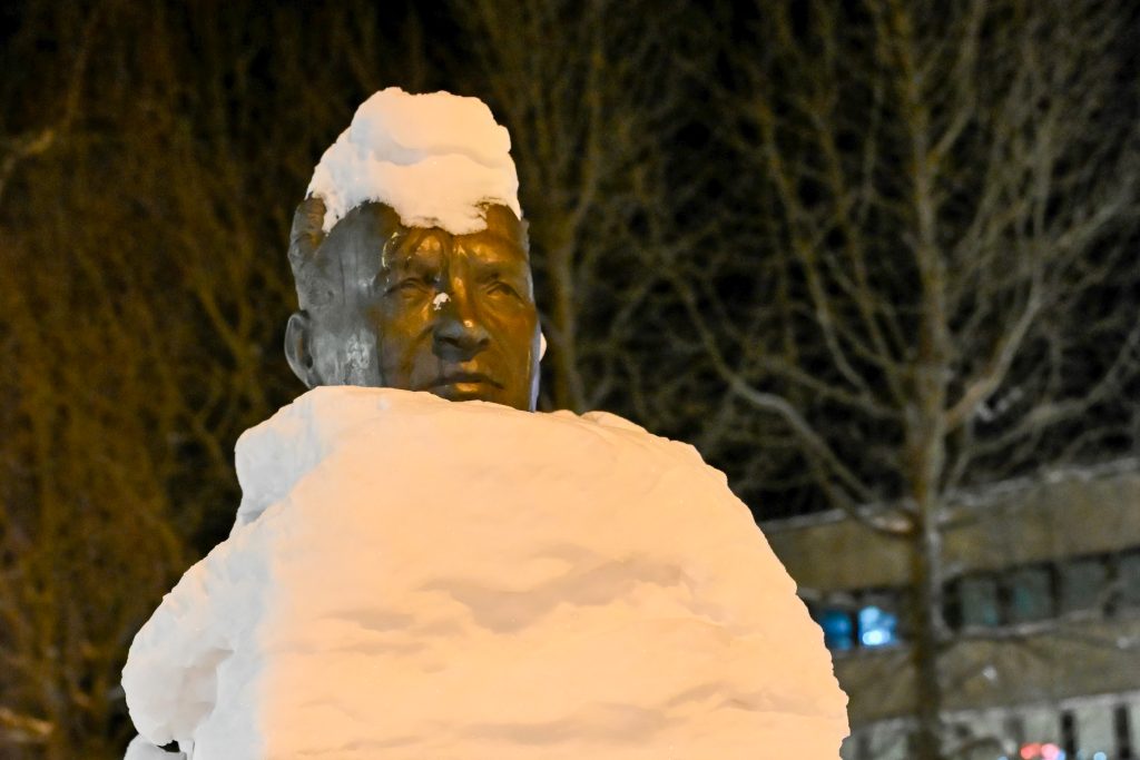 Statue with covered in snow with snow on top of head. Just a male's face is visible
