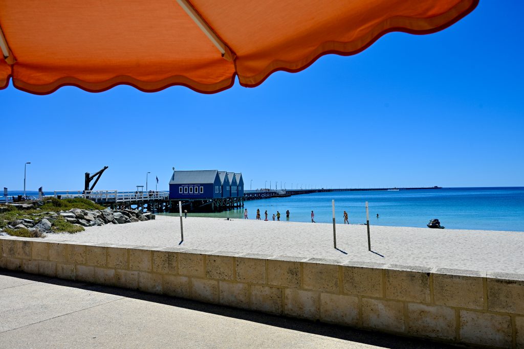 Looking out over a long wooden pier over turquoise water. Orange sun parasol at the top
