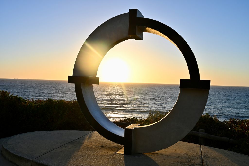 Circular sculpture with the ocean and sunset behind it.