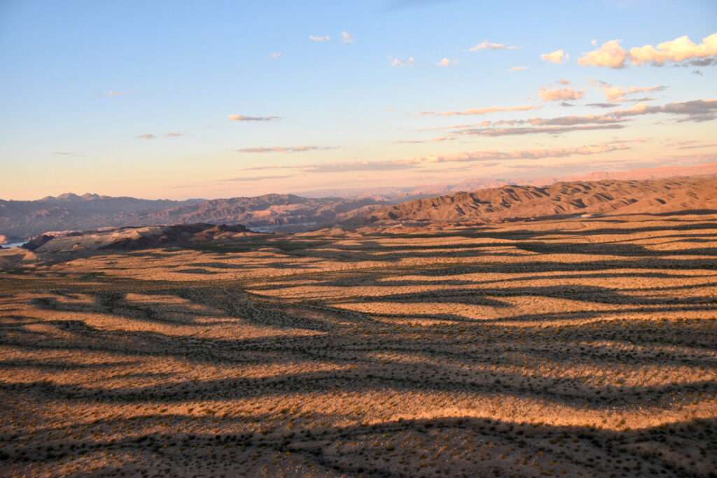Looking across a vast rocky landscape of red rocks lit up at golden hour. Pale blue sky above