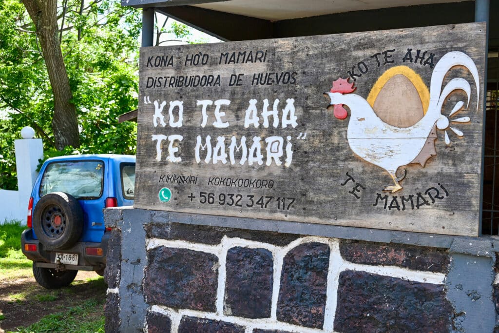 Sign for eggs for sale on a wooden board above a black brick wall. Blue car to the left