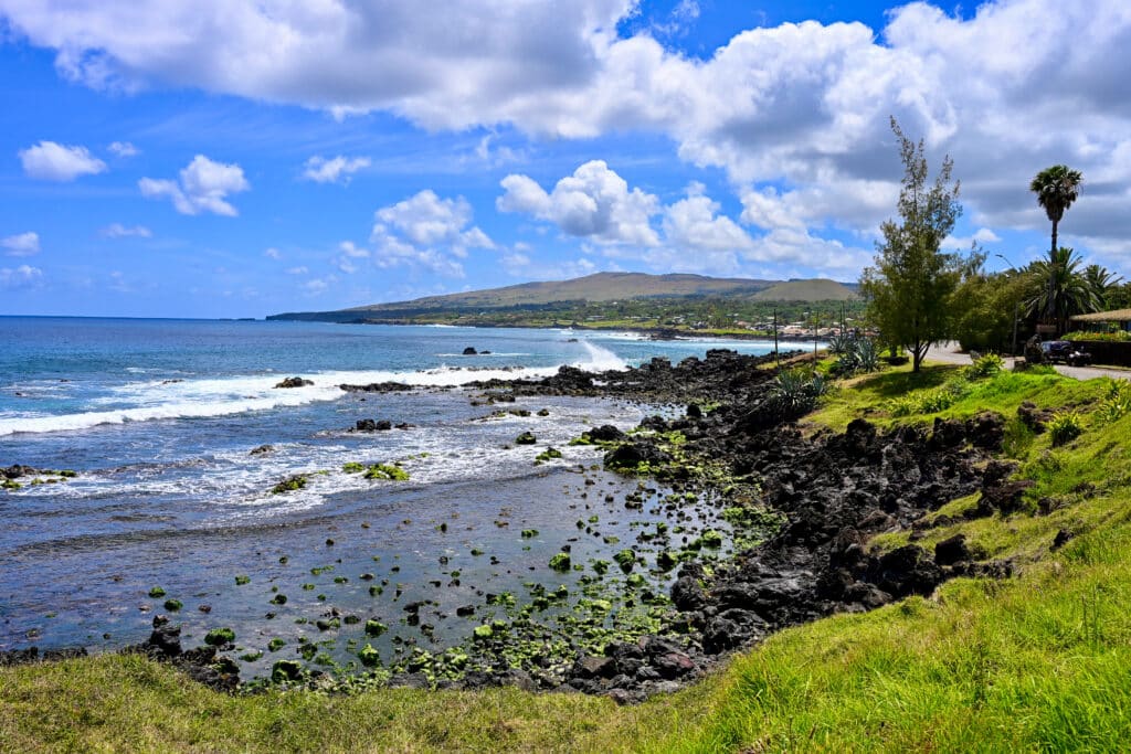 A view from the grass cliff over a rocky coast with turquoise sea. hills to the right. Blue sky above.