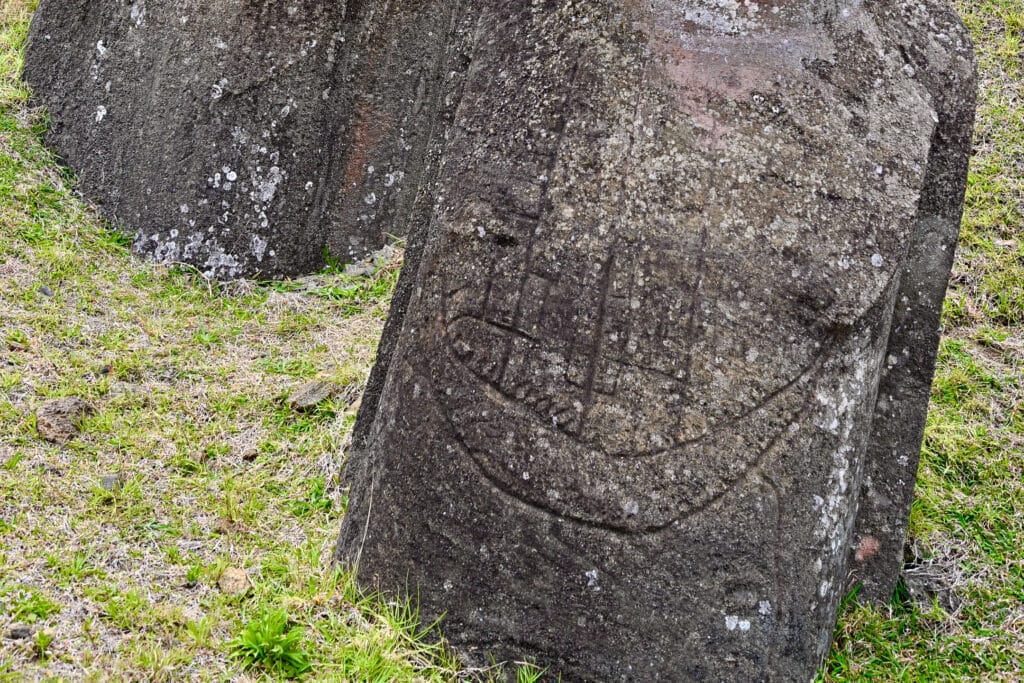 View of a carving on a stone statue - the carving looks like the hull of a ship with sails. Grass around the base of the statues
