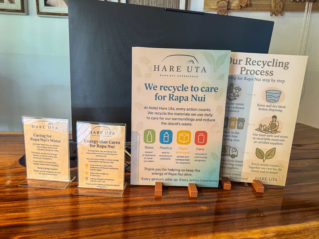 Wooden table with 4 printed information signs sitting on top. They are for Hare Uta and talk about caring for Rapa Nun's water, energy and recycling