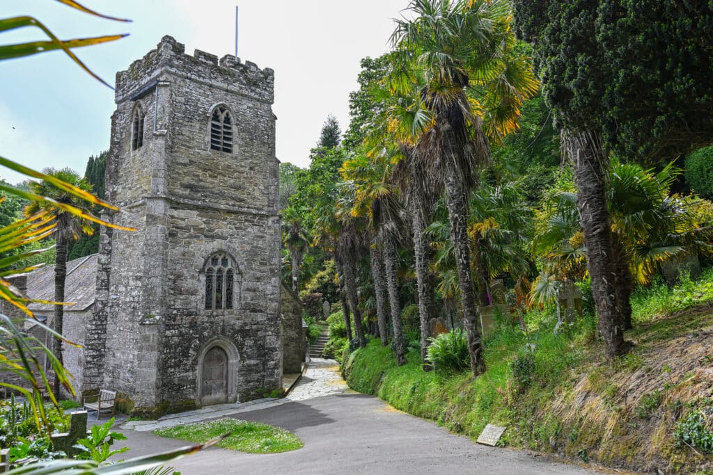 A grey stone church stands to the left hand side with a line of tall green palm trees to the right hand side. Grey sky above.