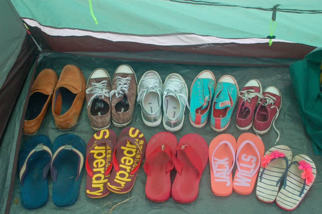 Two rows of shoes lined up in a green tent - trainers and flip flops