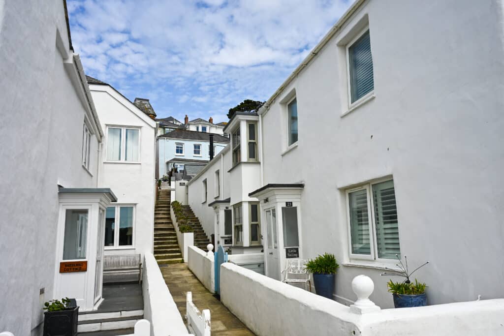 looking down a passageway with steps up a hill. White washed two storey houses on either side. A minty green house stands at the top of the stairs. Blue sky with white cloudy above.