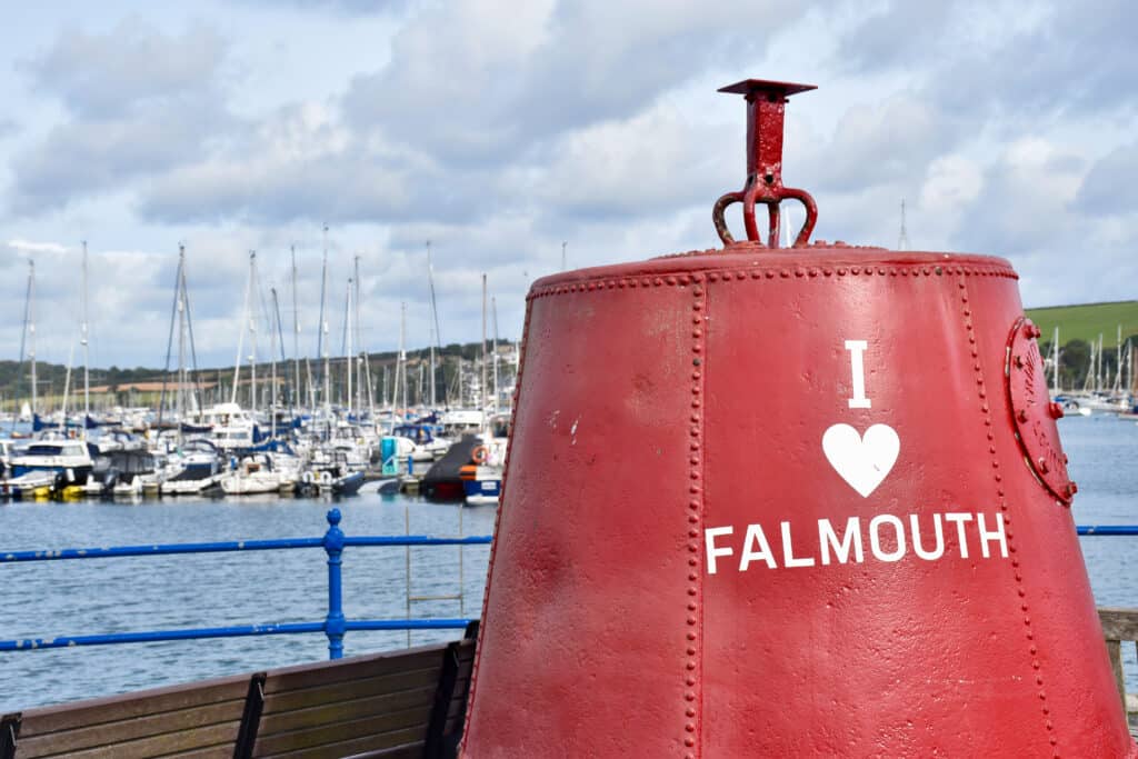 A red metal buoy sits to the right of a harbour with boats in the background