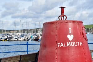 A red metal buoy sits to the right of a harbour with boats in the background