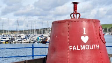 A red metal buoy sits to the right of a harbour with boats in the background