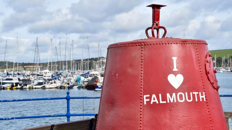A red metal buoy sits to the right of a harbour with boats in the background