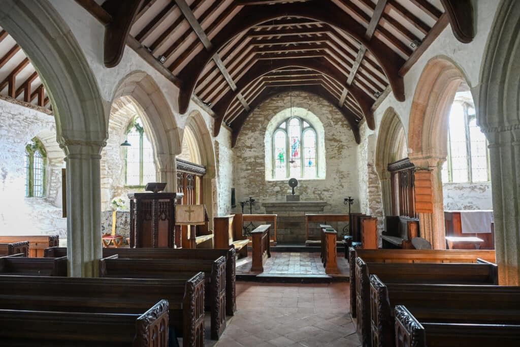Inside a small stone church with wooden ceiling, pews and arches.