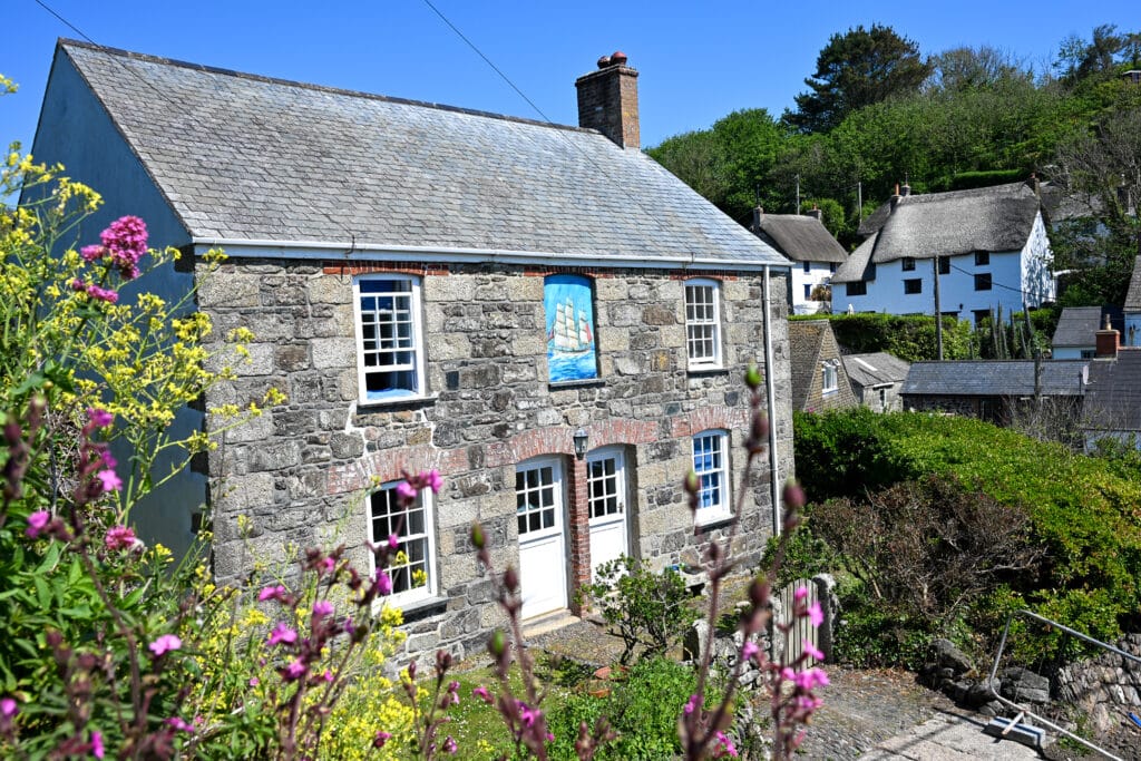 Stone cottage with painted sailboard plaque above the two doorways. Thatched cottages behind.