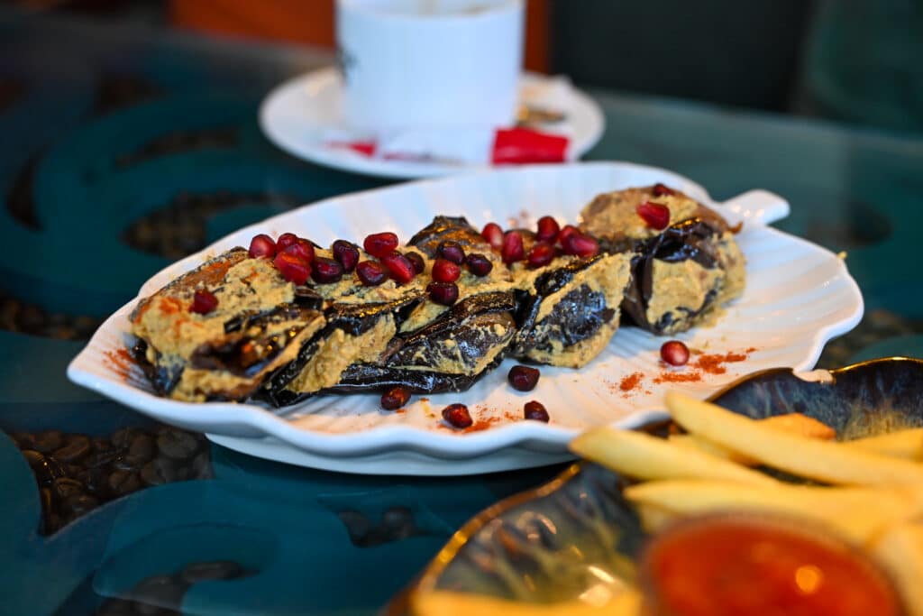 White plate shaped like a palm leaf with sliced aubergine and pomegranate seeds