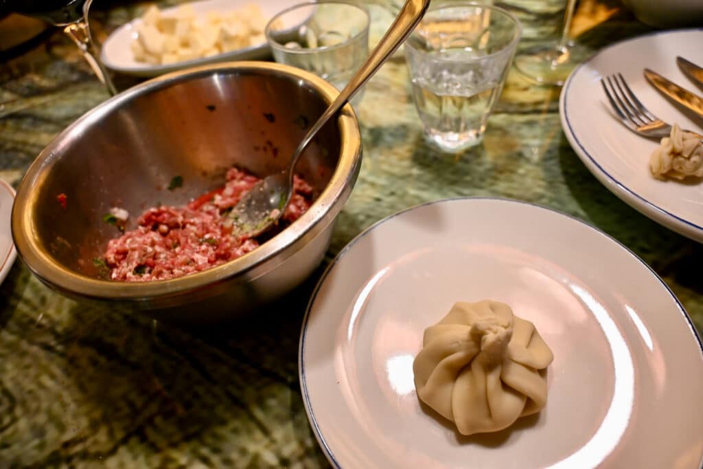 A metal bowl with mince beef mix and a white plate with single dumpling on it.
