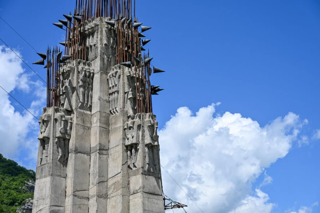Close up of a stone monument featuring carved soldiers and topped with iron spears. Blue sky