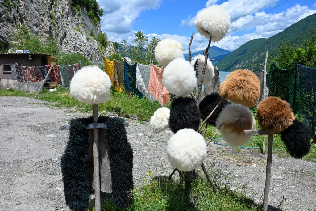 Sheepskin hats (black, white and brown) displayed on wooden posts in front of lake view