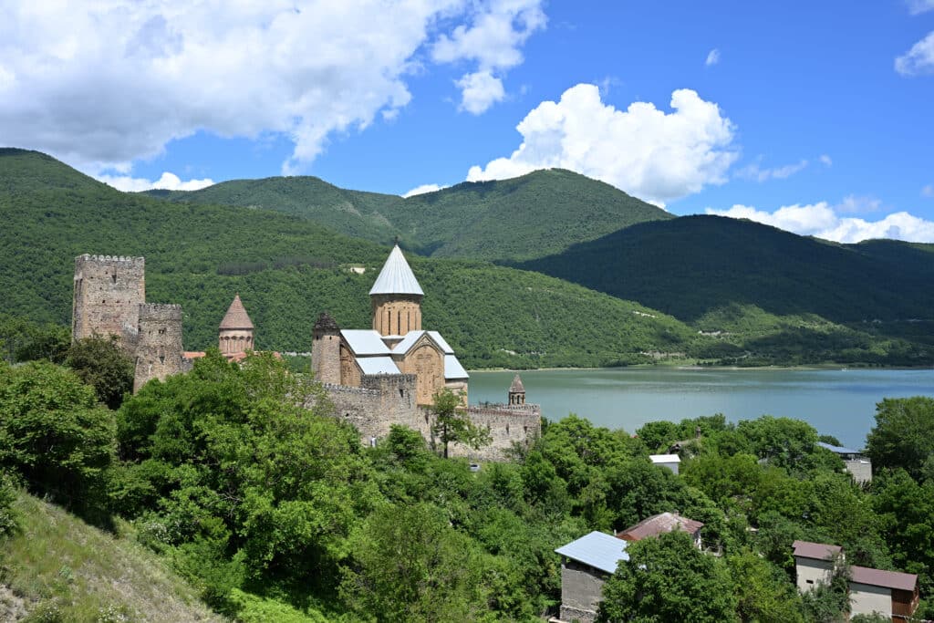 View of a fortress on a hillside overlooking a blue lake. Trees on hills